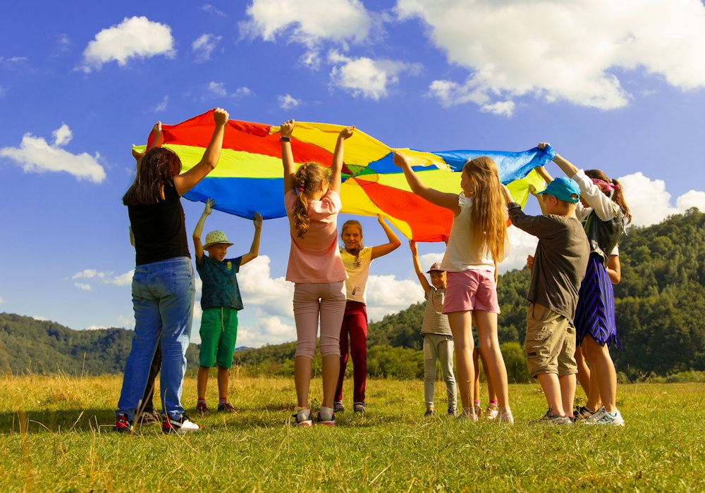 Children playing with a rainbow parachute in a sunny park